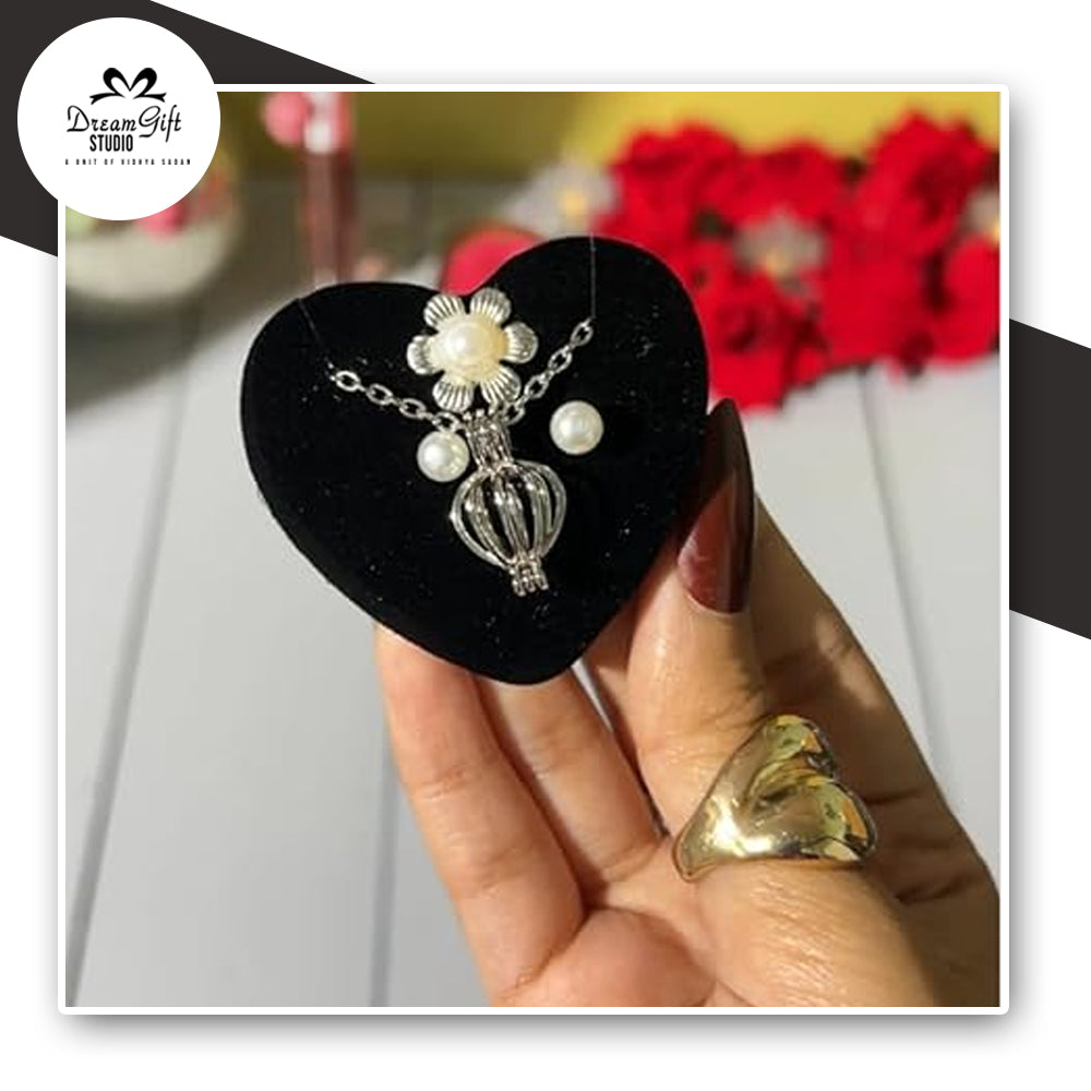 Silver necklace with pearl earrings & ring on a black heart-shaped stand held by a hand.