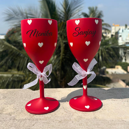 A pair of red wine glasses that can be customised with names . the glasses are bright red with white hearts on them making them look amazing